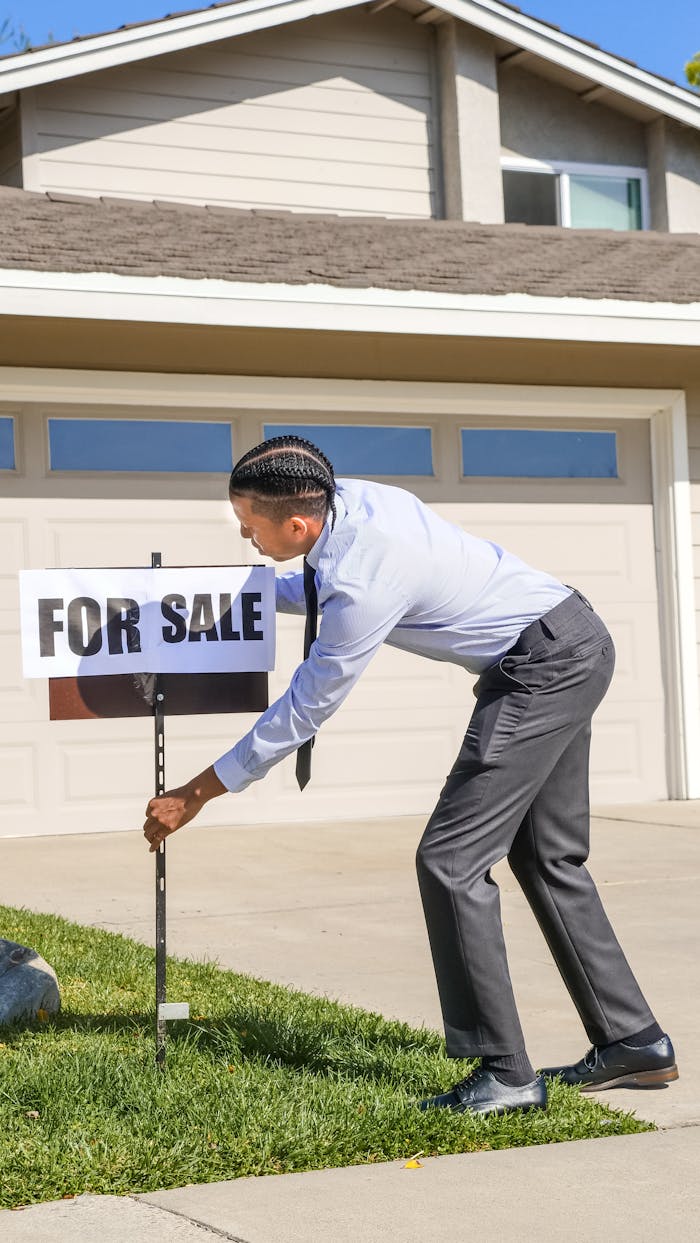 Black male realtor placing For Sale sign in front of a suburban house.